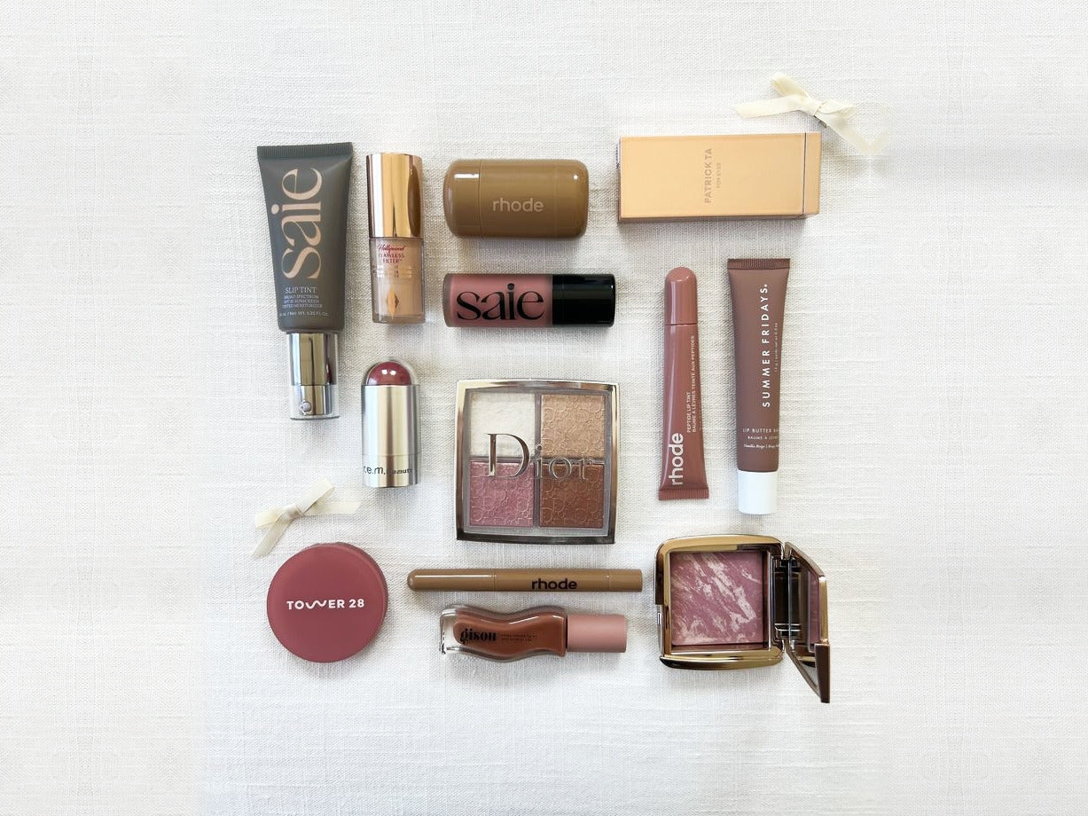 Productos de maquillaje y skincare de Saie, rhode, Dior, Patrick Ta, Summer Fridays, Tower 28 y Hourglass sobre un fondo de lino claro